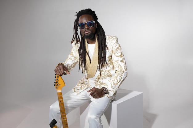 retrato de un elegante hombre africano en un traje blanco y gafas de sol con una guitarra eléctrica