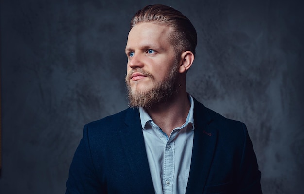 Retrato de un elegante hombre barbudo rubio vestido con un traje sobre fondo gris.