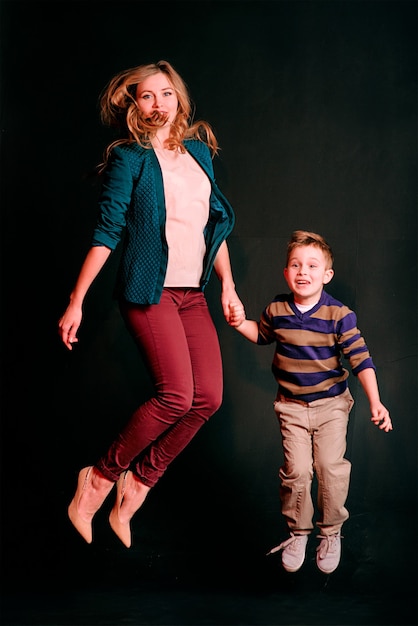 Retrato de elegante niño lindo con hermosa mamá saltando en estudio fotográfico