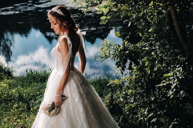 Retrato de una elegante novia con un vestido blanco con un ramo de flores en la naturaleza en un parque natural.Modelo en un vestido de novia y guantes y con un ramo de flores.