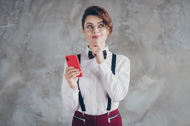 Retrato de ella, bonita, atractiva, encantadora, muy linda, creativa, inteligente, alegre, alegre, chica de cabello ondulado, usando una celda que crea una estrategia de smm aislada sobre un fondo de pared industrial de hormigón gris