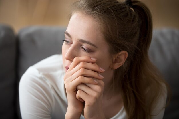 Retrato em close de mulher triste pensando sozinha sentada no sofá em casa Menina se sente infeliz e deprimida tem um problema nos relacionamentos coração partido depois de romper ou brigar com o conceito de namorado