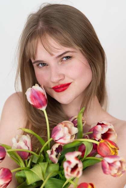 Foto retrato em close-up de mulher segurando um buquê de tulipas coloridas e cobrindo seu peito com flores