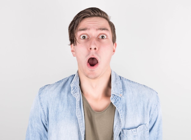 Foto retrato em close-up de um homem assustado com a boca bem aberta e os olhos em uma camisa jeans em um fundo branco