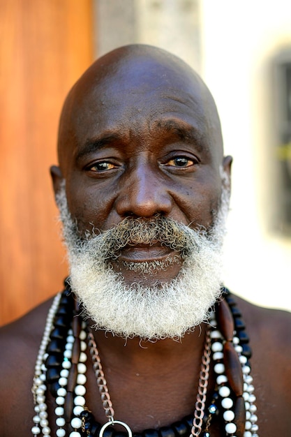 Retrato em close-up de um homem idoso careca barbudo usando vários colares ao ar livre