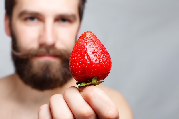 Foto retrato em close-up de um jovem segurando um morango e sorrindo