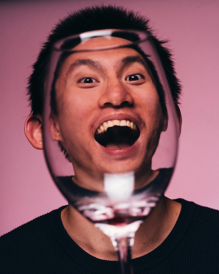 Foto retrato em close-up de um jovem visto através de um copo de vinho contra um fundo rosa