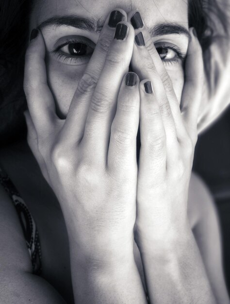 Retrato em close-up de uma jovem cobrindo o rosto com as mãos