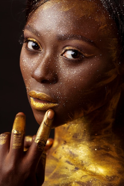 Retrato em close-up de uma jovem com brilho dourado contra fundo preto