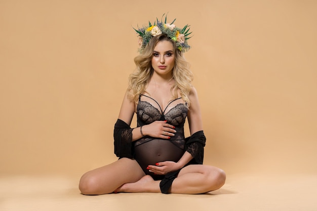 Retrato em close-up de uma linda mulher grávida em uma cueca preta translúcida com uma coroa de flores naturais na cabeça