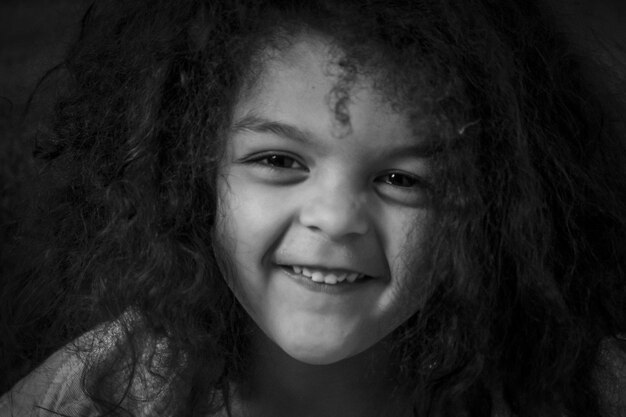 Foto retrato em close-up de uma menina sorridente contra um fundo preto