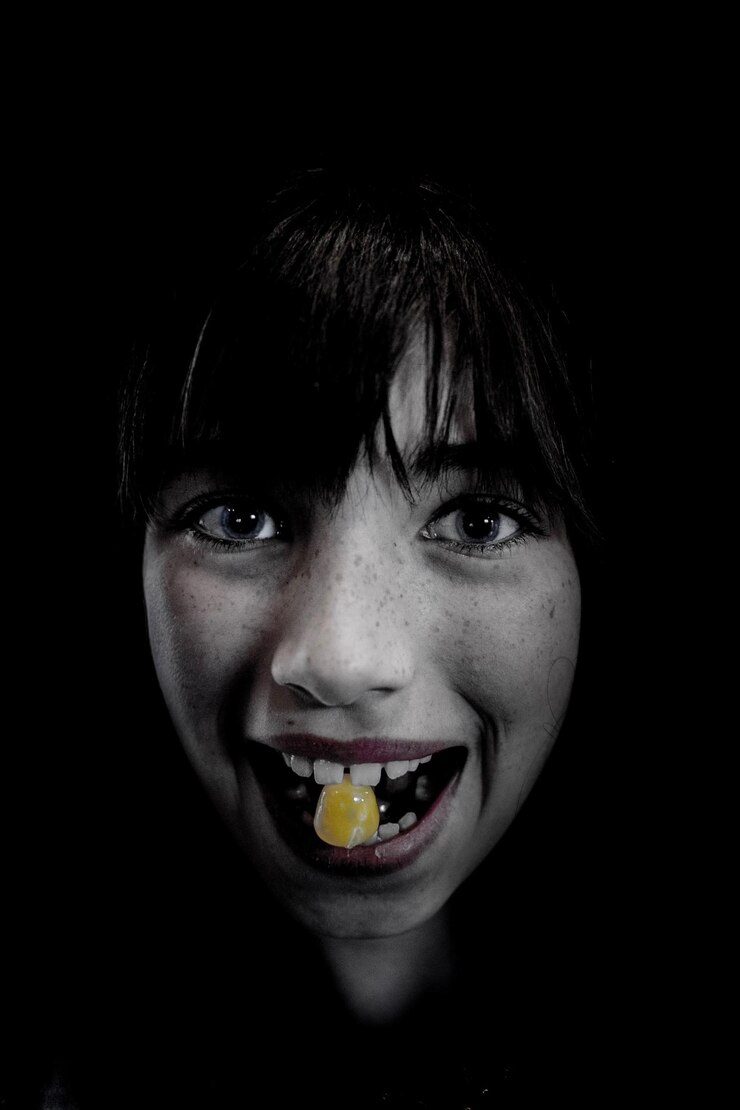 Foto retrato em close-up de uma menina sorridente segurando doces na boca contra um fundo preto