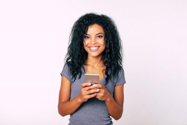 Retrato em close-up de uma mulher afro com sorriso largo e atraente e cabelo comprido e crespo, que expressa felicidade ao ler algo em seu smartphone