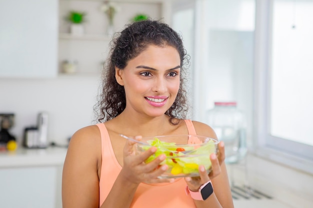 Retrato em close-up de uma mulher atraente comendo salada fresca na cozinha.