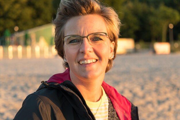 Retrato em close-up de uma mulher madura sorridente usando óculos na praia