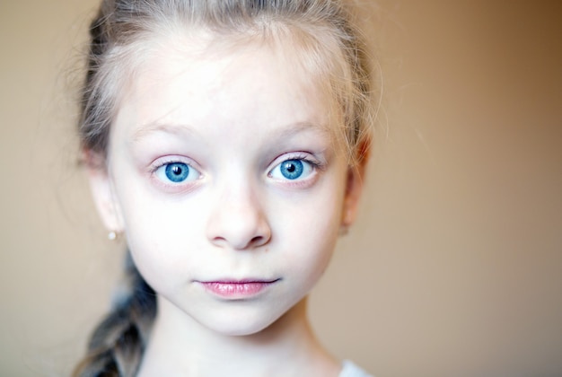 Retrato em close-up do rosto de uma linda menina de 8 anos, com grandes olhos azuis e cabelos loiros, emocionalmente olhando para o quadro