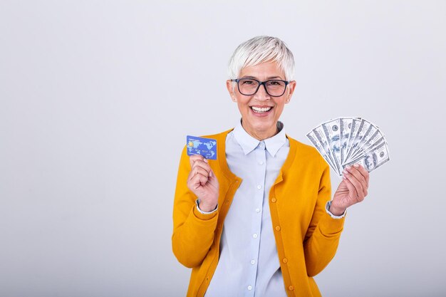 Foto retrato em close-up super feliz excitado mulher idosa bem-sucedida aposentada segurando dinheiro notas de dólar e cartão de crédito na mão emoção positiva expressão facial sentimento de compras on-line