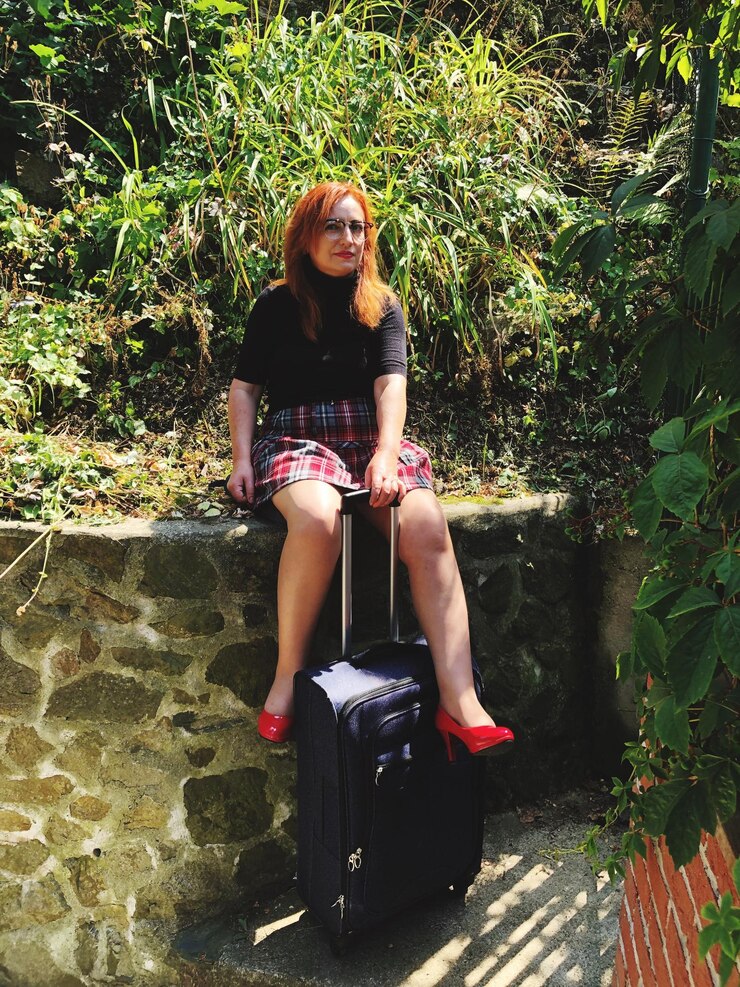 Foto retrato em comprimento completo de mulher com bagagem sentada em uma parede de suporte