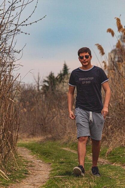 Foto retrato em comprimento completo de um jovem caminhando por uma calçada contra plantas