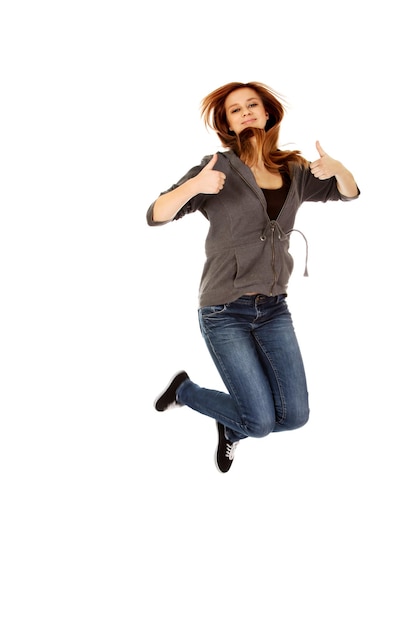 Foto retrato em comprimento completo de uma jovem mostrando os polegares para cima enquanto salta contra um fundo branco