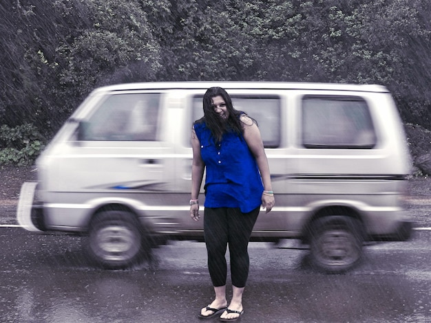 Foto retrato em comprimento completo de uma mulher de pé na frente de um carro em alta velocidade em um dia chuvoso