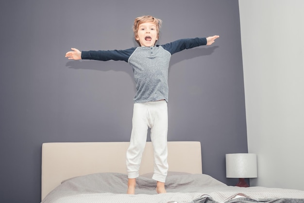 Retrato em comprimento de um menino pulando na cama em casa