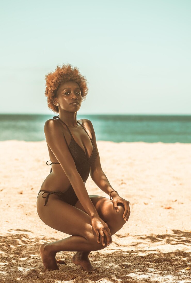Foto retrato em comprimento de uma jovem vestindo biquíni agachada na praia