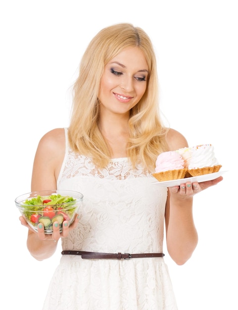 Retrato em meio comprimento de uma mulher muito bonita segurando um pequeno bolo de legumes frescos Uma jovem dona de casa escolhendo doces ou comendo bolo e salada saudáveis Isolado em fundo branco