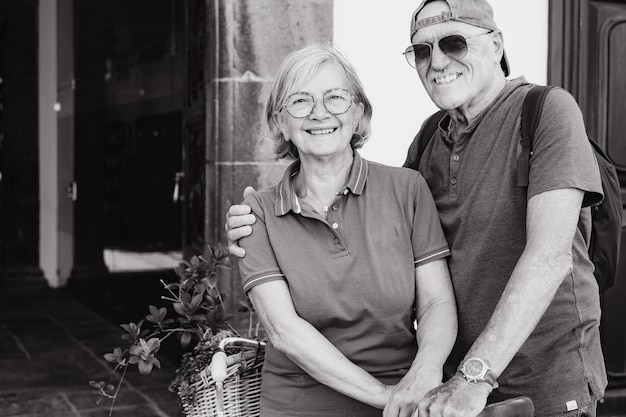 Retrato em preto e branco de um casal de idosos alegre olhando para a câmera sentado ao ar livre na bicicleta