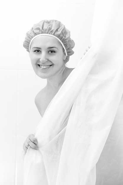 Retrato em preto e branco de uma linda mulher sorridente tomando banho e olhando por trás da cortina