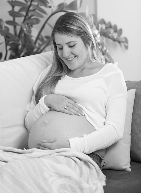 Retrato em preto e branco de uma mulher grávida sorridente, deitada no sofá e tocando a barriga