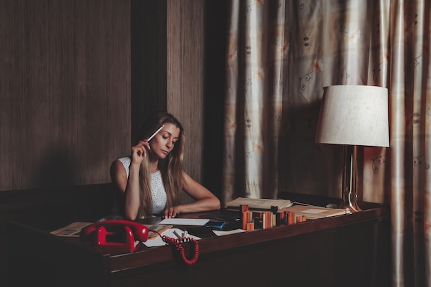 Retrato emoción mujer adulta actriz con periódico viejo trabajando vestida con ropa de estilo retro en la oficina de la vendimia. Mujer en vestido blanco y negro de estilo pin-up en lunares trabaja por la noche