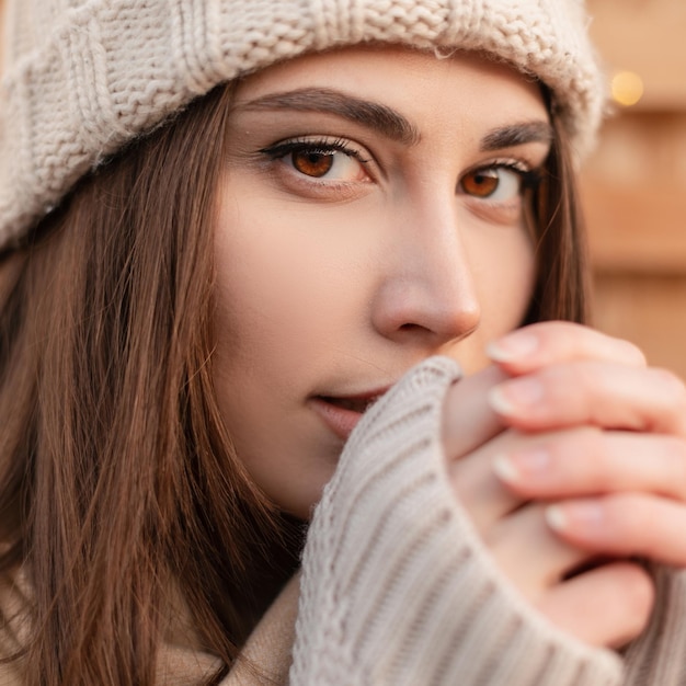 Retrato emocional de uma linda jovem bonita com olhos castanhos em roupas da moda com chapéu de malha e suéter vintage bege ao ar livre