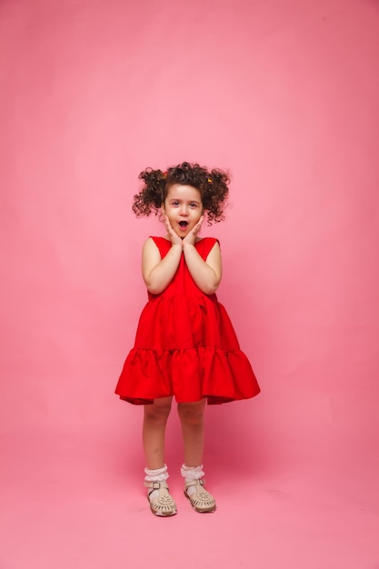 Retrato emocional de uma menina em um vestido vermelho em um fundo rosa