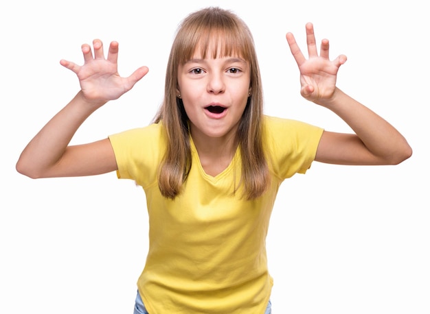 Retrato emocional em meio comprimento de uma menina caucasiana vestindo uma camiseta amarela Uma criança engraçada engraçada olhando para a câmera com as mãos em um gesto assustador isolado em fundo branco