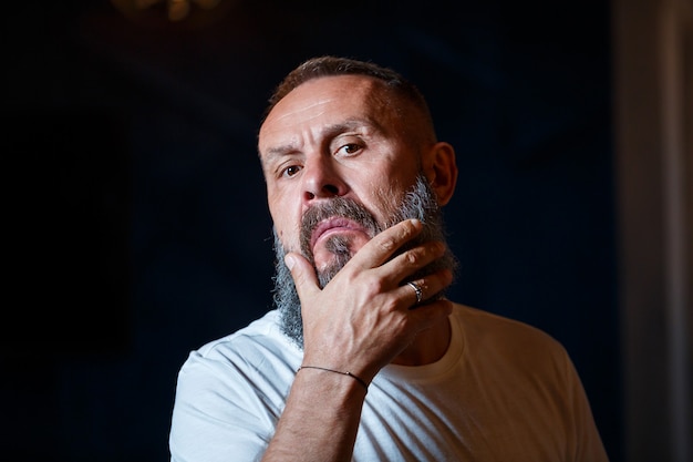 Retrato emocional de un hombre adulto de pelo gris con barba en una camiseta blanca