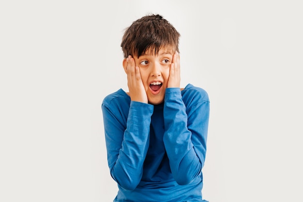 Retrato emocional de medio cuerpo de un muchacho adolescente caucásico con camiseta azul. Adolescente sorprendido mirando a cámara. Niño feliz guapo, aislado sobre fondo blanco.