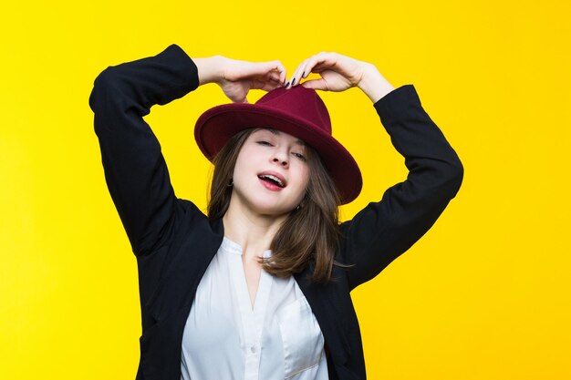 Retrato emocional de una mujer joven con traje y sombrero en un fondo amarillo