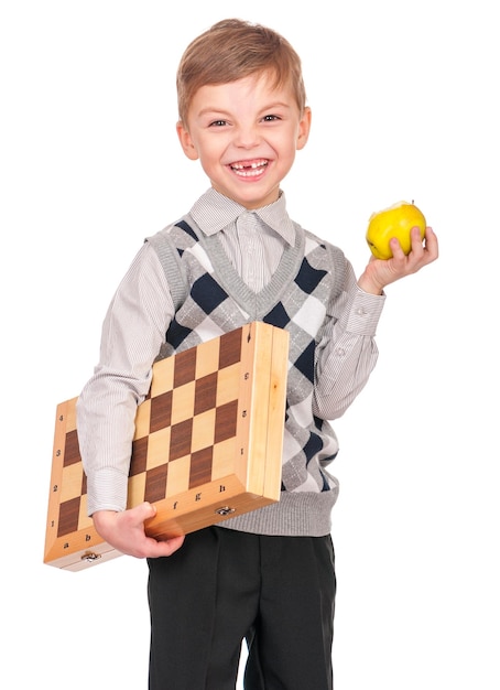 Retrato emocional de un niño caucásico con un tablero de ajedrez y una manzana Niño gracioso sosteniendo una partida de ajedres en sus brazos mientras se ríe Niño lindo e inteligente aislado sobre un fondo blanco