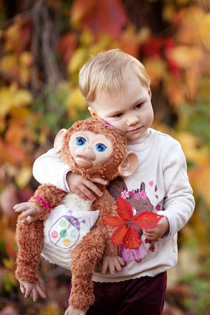 Retrato emocional outono da menina. Menina bonita com brinquedo de macaco no parque outono. Atividades de outono para crianças. Dia das Bruxas e diversão de tempo de Ação de Graças para a família.