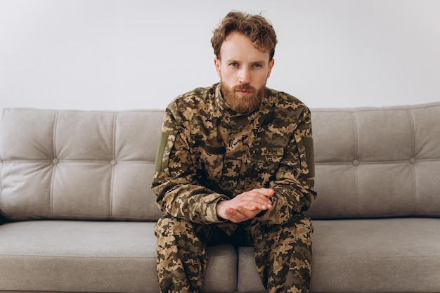 Retrato de un emotivo joven soldado patriota ucraniano barbudo con uniforme militar sentado en el sofá de la oficina