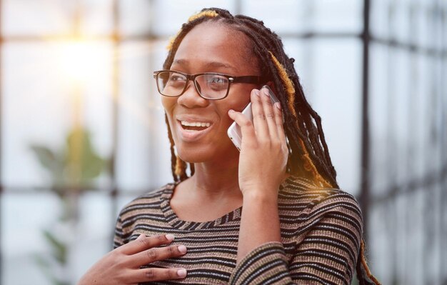 Retrato de una empleada negra de cerca con gafas trabajando en la oficina hablando por teléfono móvil resolviendo