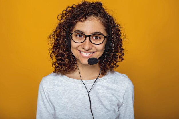 Retrato de un empleado feliz del centro de atención telefónica de la muchacha en auriculares y vidrios.