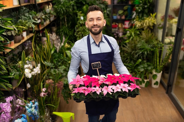 Retrato de un empleado de una floristería con pequeñas flores rojas perfectas en sus manos