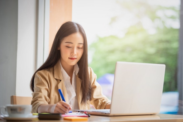 Retrato de la empresaria asiática joven que se sienta dentro en café usando la tableta digital con café. Concepto de éxito empresarial.