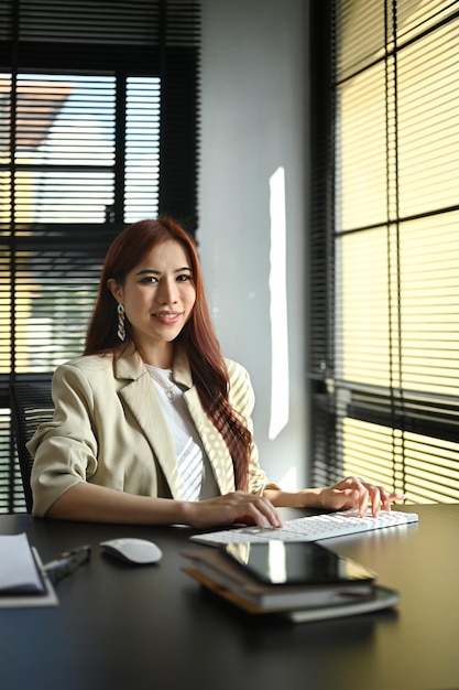 Retrato de una empresaria milenaria con traje elegante sentada en su lugar de trabajo y sonriendo a la cámara