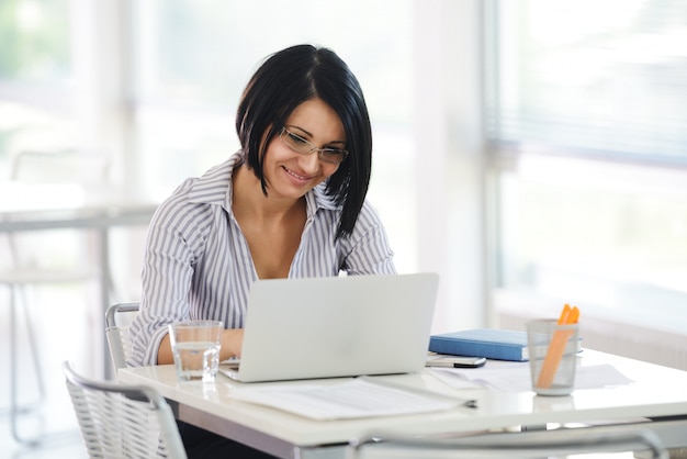 Retrato de una empresaria que trabaja que se sienta en su escritorio con una computadora portátil que parece feliz