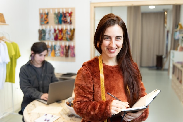 Retrato de una empresaria sastre sonriente escribiendo en un cuaderno en su estudio