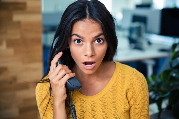 Retrato de una empresaria sorprendida hablando por teléfono en la oficina