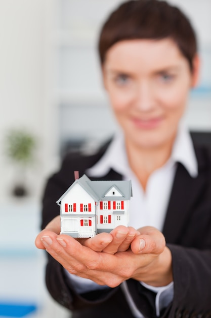 Foto retrato de una empresaria sosteniendo una casa en miniatura